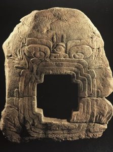 Large olmec stone carving against a black background. It is in the shape of an earth monster with a cross shaped mouth. It is the piece described in the main body text.
