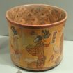 Maya ceramic vase that is painted with male figures sitting crosslegged holding a basket.