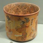 Maya ceramic vase that is painted with male figures sitting crosslegged holding a basket.